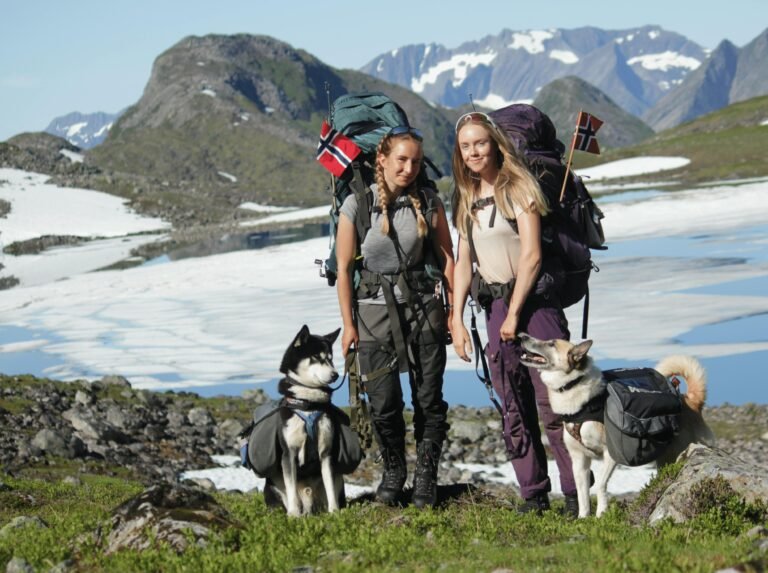 Two young women hiking with dogs in the scenic Norwegian mountains during summer.